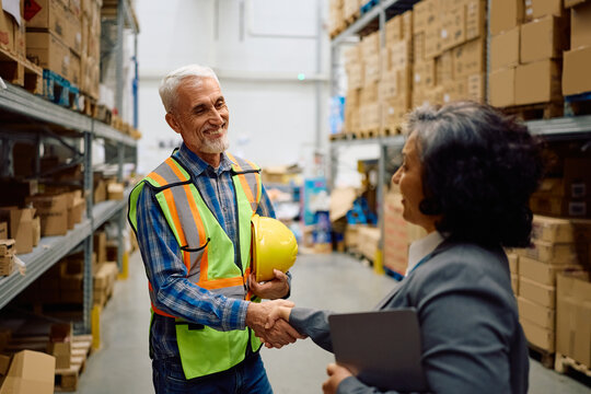 Happy senior warehouse worker greeting his manager at storage compartment.