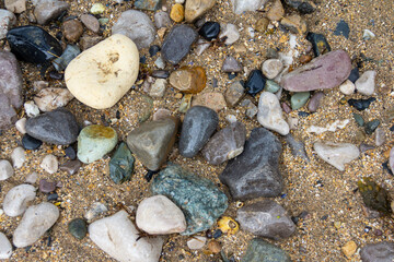 Wet pebbles, stones and sand on the beach, forming an abstract image of nature at the seaside.