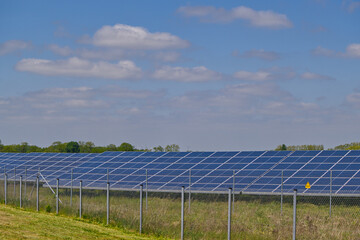 Northern German solar farm, a field full of solar panels is protected by a fence with a warning sign