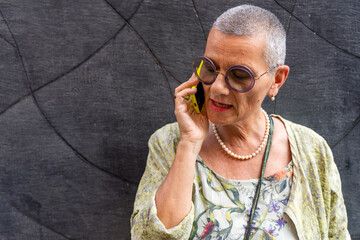 beautiful mature woman with shaved gray hair talking on cell phone in front of black wall