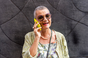 beautiful mature woman with shaved gray hair talking on cell phone in front of black wall