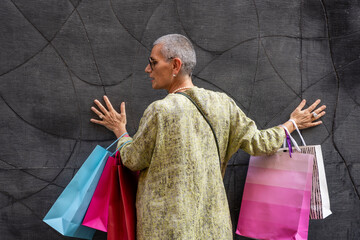 elegant mature woman with colorful shopping bags posing with her back turned in front of a black wall