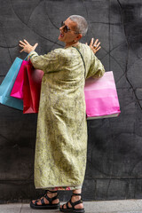 elegant mature woman with colorful shopping bags posing with her back turned in front of a black wall