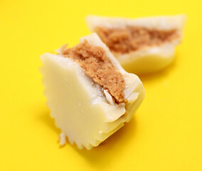 halved white chocolate bonbon on yellow background, sweet food theme