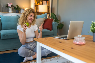 Young woman in athletic outfit doing fitness workout at home, following virtual trainer via laptop...