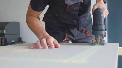 Worker in overalls using handheld electric jigsaw to cut wooden board. Man working in home garage workshop. Home selfmade renovation and DIY concept - Powered by Adobe