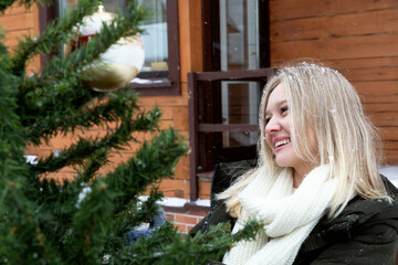 A young blonde woman smiling decorates a Christmas tree outside