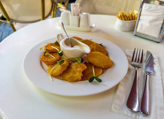 Crispy golden potato latkes (draniki, deruny) with sour cream on a white table in a summer cafe.Delicious plate of potato fritters for brunch, served with a creamy dip in a ceramic sauceboat