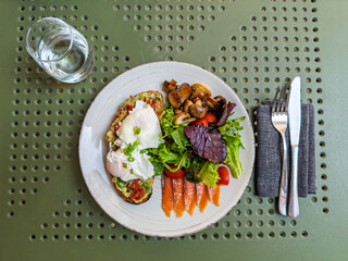 Delicious Eggs Benedict served with a side salad on a rustic plate for a perfect outdoor brunch on a summer day.Close-up of a gourmet brunch plate. Poached eggs on toast with fresh salad and cutlery