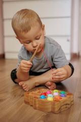 Baby boy playing with wooden fishing toy while sitting on floor at home. Educational activity for fine motor skills development.
