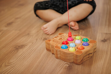Boy playing with wooden fisherman toy sitting on the floor at home. Close-up. Educational activity for fine motor skills development.