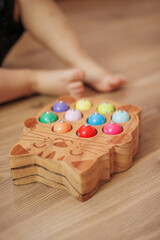 Boy playing with wooden fisherman toy sitting on the floor at home. Close-up. Educational activity for fine motor skills development.