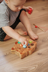 Baby boy playing with wooden fishing toy while sitting on floor at home. Educational activity for fine motor skills development.