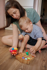 Obraz premium Mother and toddler playing together with a wooden fishing toy at home. Early childhood development and parent-child bonding activity indoors.
