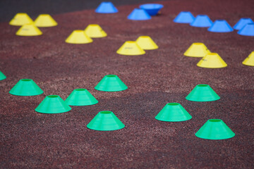 Brightly colored plastic training cones arranged on a textured sports surface, used for agility...