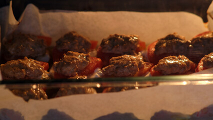 Close-up shot of ground meat patties placed on parchment-lined tray, slowly cooking inside an oven under warm lighting.