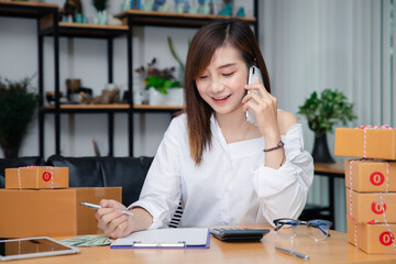 Woman are receiving orders via cell phone. Successful entrepreneur business woman with online sales and Parcel shipping in her home office. Business owner talking on mobile phone and using laptop.