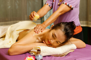 Masseuse drips warm massage oil from a candle on the back of the young woman.