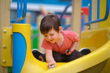 Little boy playing with toy car on a yellow slide at outdoor playground. Happy child on vacation enjoying summer activity. A child aged 3 years © Андрей Журавлев