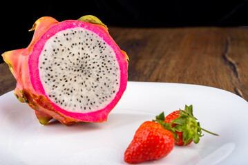 Half a pitahaya or dragon fruit on a plate with strawberries.