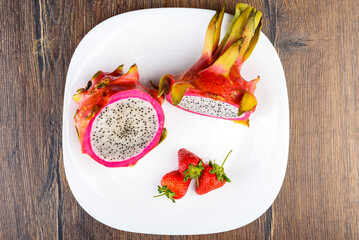 Top view of two halves of Dragon fruit or Pitaya and three strawberries on a white plate.