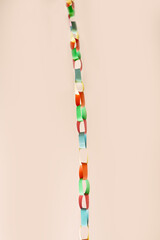Vertical chain of interlinked colorful paper rings suspended against soft beige background. This vibrant handmade garland , childhood creativity, festive decor, crafting with simple materials