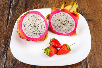 Close-up of two halves of dragon fruit or pitaya and three strawberries on a white plate.