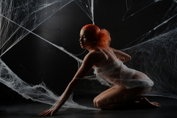 Red-haired woman trapped in a delicate web of white strands in dark setting