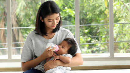 Young mother feeding baby with bottle while holding infant on lap in peaceful home environment