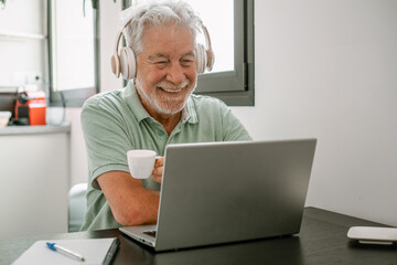 Video call concept.  Senior caucasian smiling businessman sitting at home desk working online on laptop, enjoying a coffee cup