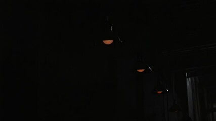 Row of industrial pendant lights illuminating a dark corridor with textured walls - Powered by Adobe