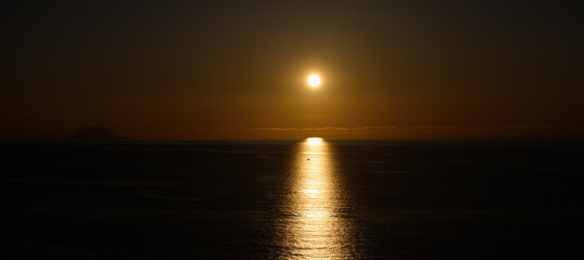 Sun setting over the Tyrrhenian Sea, with Stromboli Volcano visible in the distance, near Tropea, Calabria, Italy
