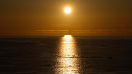 Sun setting over Tyrrhenian Sea reflecting on water surface, creating golden path, with few boats sailing, near Tropea, Calabria, Italy