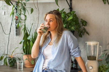 Young woman drinking healthy green smoothie on home kitchen.