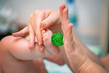 Mother performing a gentle foot massage on her baby using a green plastic Su-Jok ball, promoting relaxation and bonding
