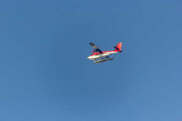 Red and white seaplane soars against a clear blue sky
