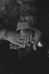 Black and white photo of intergenerational hands stacked together, symbolizing family, love, protection, and unity. Tender emotional moment.