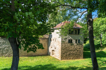 A tranquil, sun-drenched historic wall with a tower, surrounded by green trees and grass.