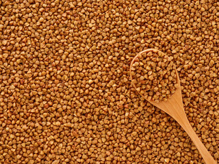 Raw buckwheat background and wooden spoon with cereal on top. Texture brown grains pattern. Healthy food. Top view overhead.
