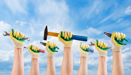 Hands of mans workers holds different tools hammer, wrench, screwdriver, pliers in gloves against background blue sky with clouds. Labor day concept. Holiday background.