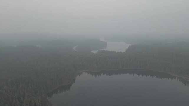 Drone based aerial looking down on an evergreen forest and small lakes covered in thick forest fire smole.