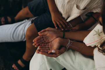 Close-up of family hands gently overlapping in warm natural light. Concept of care, bonding, love, and connection in a relaxed, summery setting.