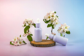bottle of essential oil with a pipette and a blooming apple tree branch on a wooden podium on a gradient background. The concept of skin care using natural cosmetics