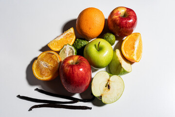 Mixed fresh fruits with apples, oranges, kaffir limes, and vanilla pods on white background