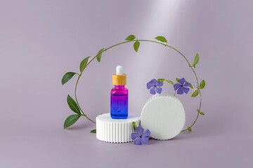 bottle of essential oil with a pipette and periwinkle flowers on a white podium on a purple background. The concept of skin care using natural cosmetics
