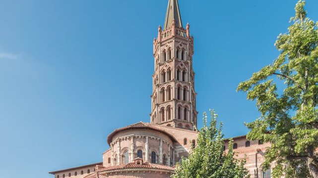 The cobbled parvis of the Basilica of Saint Sernin in Toulouse, France, timelapse hyperlapse. Largest romanesque church in Europe with brick bell tower, arched doors, green trees and blue sky