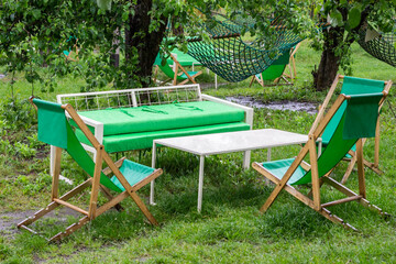Folding wooden chairs, a summer sofa and a table on a lawn in the garden. Recreation area in park.