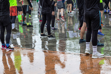 Athletes stand on a wet track during rain. Reflections of feet in puddles. Part of frame