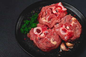 raw steak, calf's neck on the bone, fresh meat, on a black plate, top view, no people,