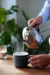 Male pouring hot water from kettle into mug in cozy kitchen setting